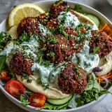 A vibrant Falafel Bowl featuring fluffy falafel, crunchy vegetables, and creamy tzatziki, served with lemon wedges. 