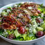 Vibrant Mediterranean-inspired Greek salad bowl topped with tender grilled chicken, drizzled with tangy lemon-oregano dressing for a refreshing meal.  