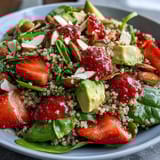 Colorful quinoa salad featuring ripe strawberries, diced avocado, and baby spinach, topped with toasted almonds and feta.  