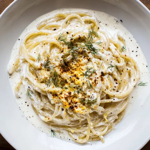 A close-up of finished Turkish Yogurt Pasta, swirled with paprika butter and fresh herbs.