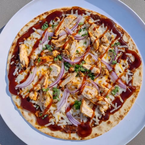 Golden, crispy-crust Chicken BBQ Pizza drizzled with barbecue sauce and garnished with fresh cilantro on a wooden board.