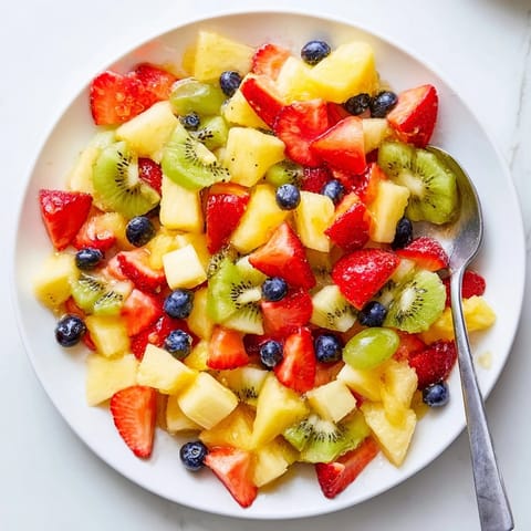 A close-up bowl of chilled Fruit Salad brimming with vibrant kiwi, blueberries, and sweet pineapple chunks.