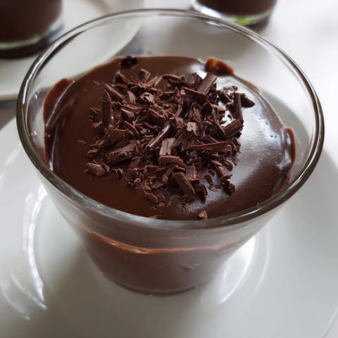 Smooth chocolate pudding set in a small bowl, garnished with delicate chocolate shavings and a mint sprig.