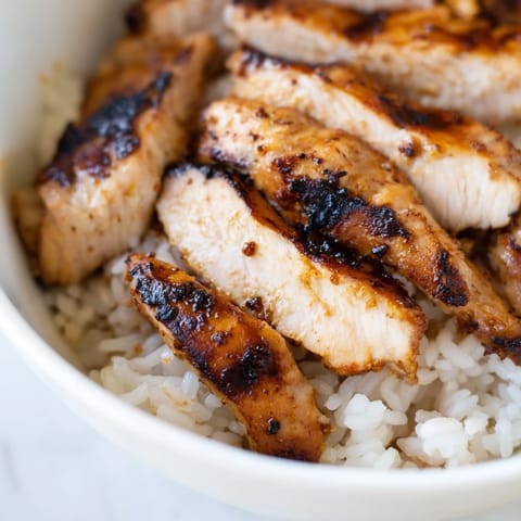 Spicy chicken burrito bowl featuring charred chicken, vibrant veggies, and melted cheese, garnished with fresh cilantro and a lime wedge on the side.