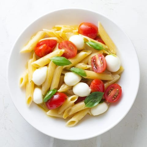 Bright, juicy cherry tomatoes, creamy mozzarella pearls, and fresh basil mingle with al dente penne pasta, all tossed in extra-virgin olive oil for a simple Caprese Salad Pasta.