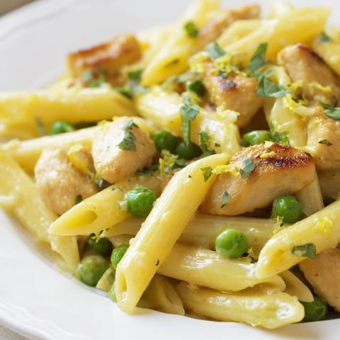 Bright green peas and tender chicken pieces nestle in penne pasta, coated in a glossy lemon-mint sauce, ready to serve.  