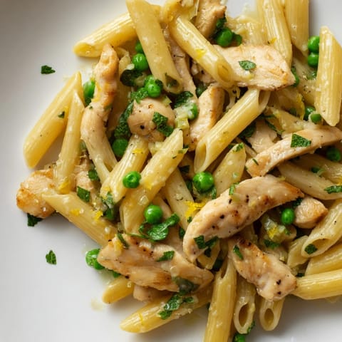 Freshly chopped mint and grated Parmesan garnish this vibrant Pea & Mint Chicken Pasta, steaming on a spring dinner table.  