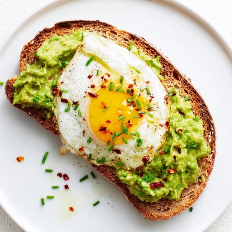 A close-up of a delicious avocado toast recipe featuring a poached egg, sea salt, and drizzled olive oil on a rustic plate.