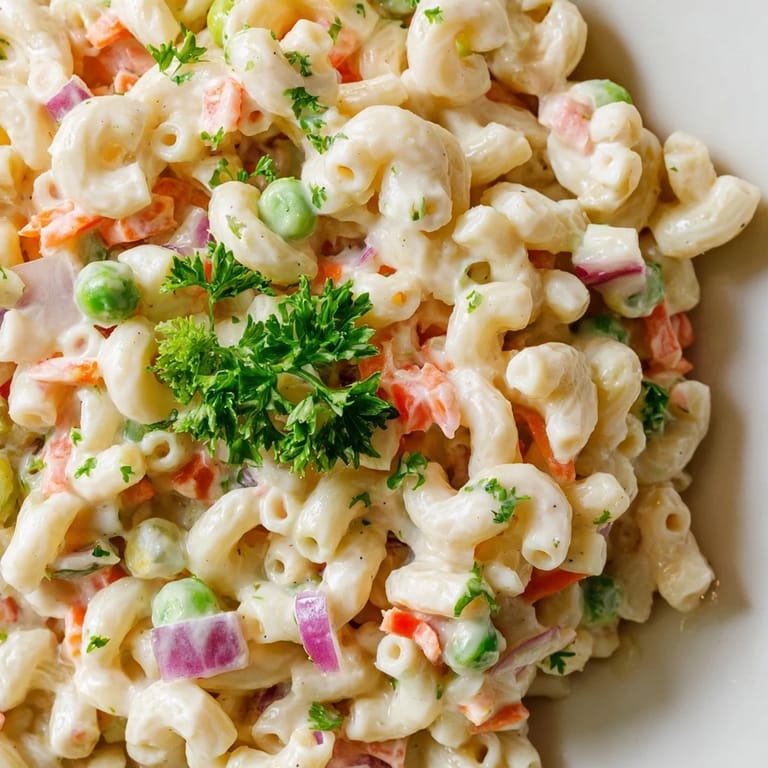Colorful Macaroni Salad featuring tender pasta, grated carrots, green peas, and a tangy mayonnaise dressing on a picnic table.
