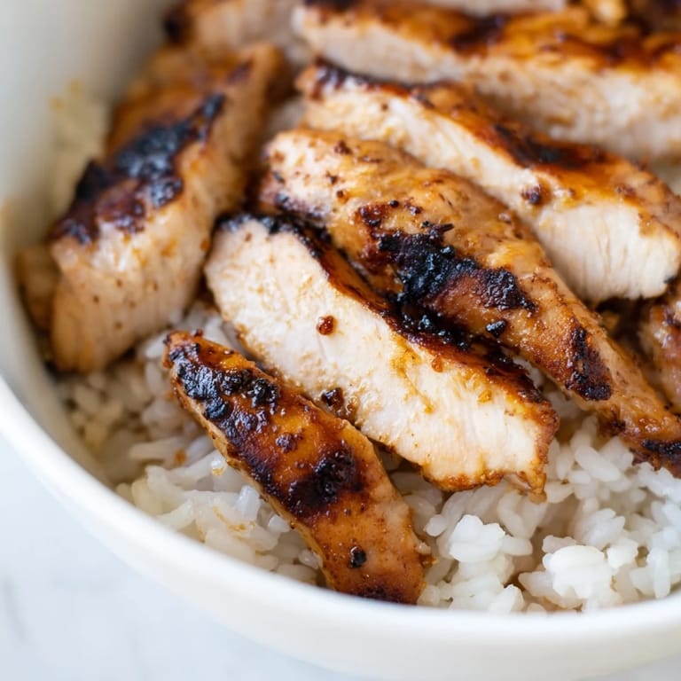 Spicy chicken burrito bowl featuring charred chicken, vibrant veggies, and melted cheese, garnished with fresh cilantro and a lime wedge on the side.