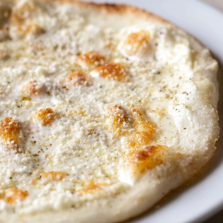 Golden-baked Creamy Garlic White Pizza on parchment, brushed olive oil crust and rich, creamy garlic sauce visible.
