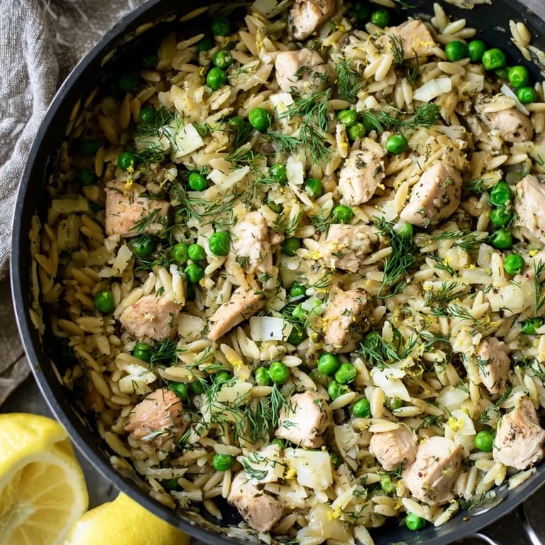 Fork-tender chicken thighs and orzo pasta simmering in a lemony herb sauce, with steam rising from the one-pan skillet.