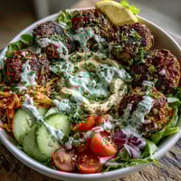 Falafel Bowl with crispy falafel on creamy hummus, fresh greens, and a drizzle of tangy tahini sauce. 
