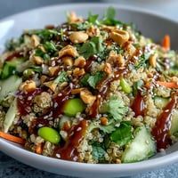 Thai Coconut Quinoa Bowl topped with crisp red peppers, carrots, and cucumber, drizzled with creamy peanut dressing and sesame seeds.